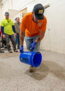 A student pouring product out of a blue 5 gallon bucket during his training for his concrete science degree
