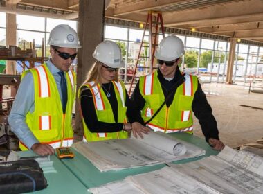A group of students gathered around blueprints on a jobsite.