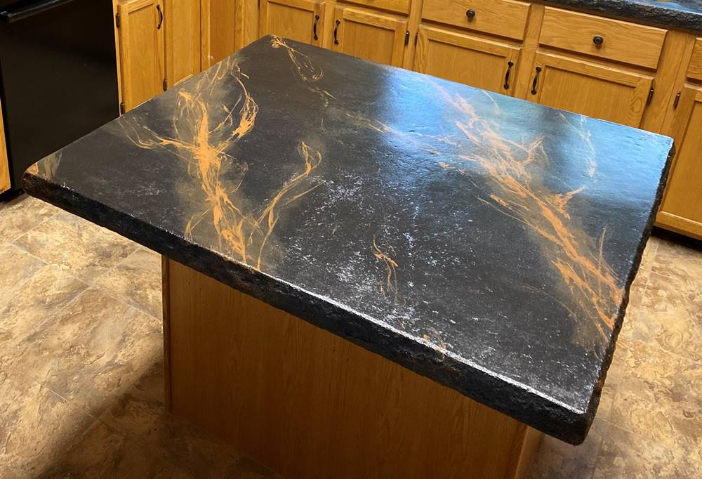 kitchen island with a concrete countertop in black with orange-ish veining.