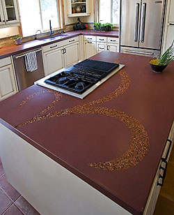 Large kitchen island with a red countertop and a decorative inlay of aggregate in a swirl pattern.