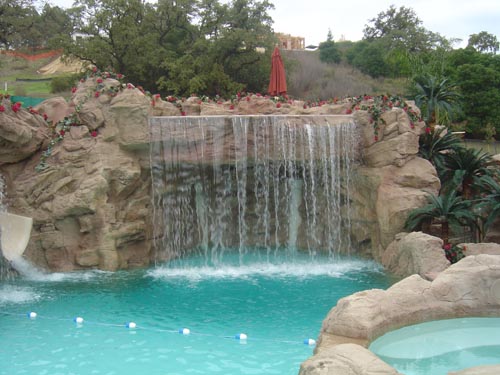 An enormous water fall was created in this backyard that flows over hand carved rocks and crashes into a bright blue pool below.