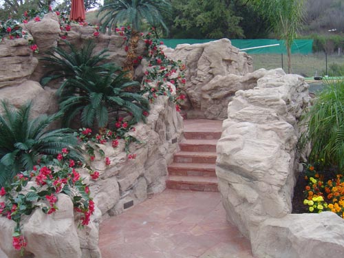 Landscaping and rock features work seamlessly together to create a concrete oasis in this backyard including steps built in to take guest to the next level of terrain.