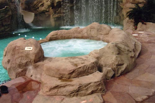 A hot tub sits just on the other side of the waterfall but blends in with the rock features surrounding it.