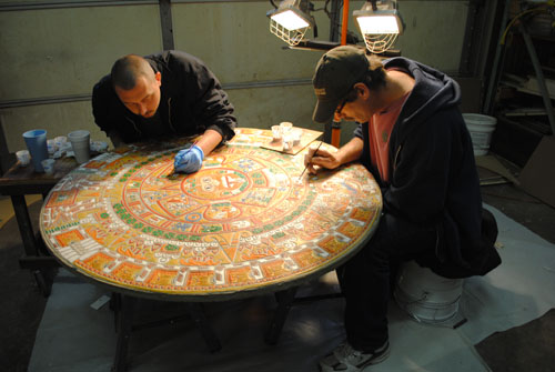 Two men work on the intricacies and detail work of staining and coloring the Aztec Calendar.