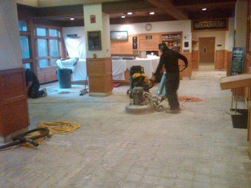 A man runs a grinding machine on a floor that removes the previously treated concrete.