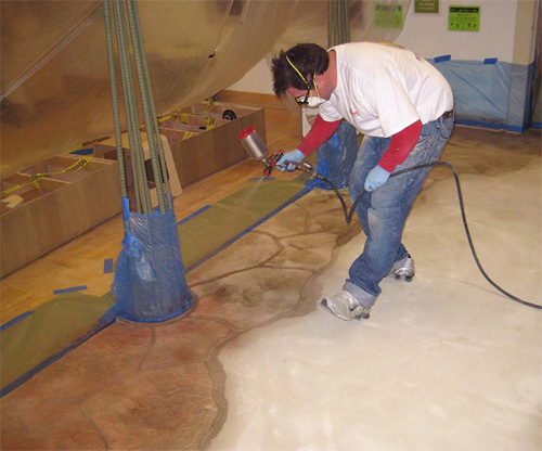 Trevor Foster of Miracote using an air paint sprayer to apply color to a concrete floor that has had a microtopping applied.
