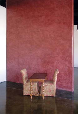 A red vertical concrete wall with two chairs and a table in front of it.
