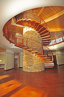 Tall spiral stair case surrounds a faux stone column above a stained concrete floor.