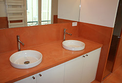 Orange concrete countertop in a bathroom with two white sinks.
