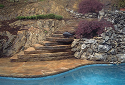 Concrete rustic steps that lead down to a blue pool.