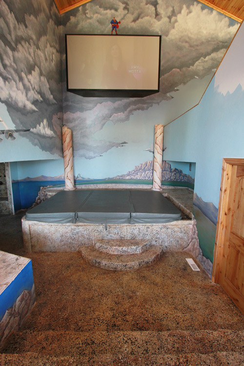 Superman painted on the wall above the hot tub in this man cave. Concrete steps lead into this space 