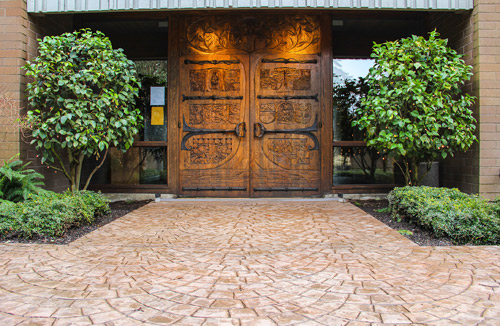 Large wooden double doors with stamped concrete leading up to it.