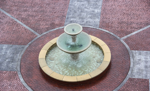 A large three tiered fountain in the center of the stamped concrete courtyard.