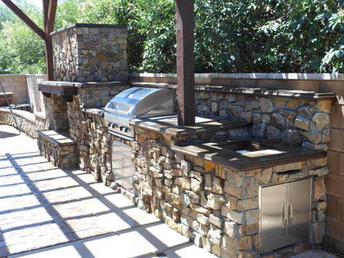 A look at an outdoor kitchen with stone facade and concrete countertops.