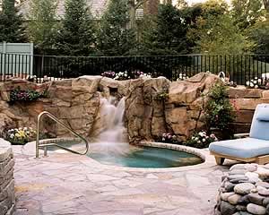 synthetic rocks from concrete surrounding a hot tub with a water fall tumbling down the faux rocks into the hot tub.