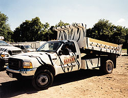 A dump truck that is painted with zebra stripes in mid dumping mode.