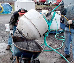 Pouring concrete mix into a wheel barrow after mixing the pigment into wet concrete in a small portable mixer.