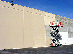 A scissor lift in front of a large outdoor building as the contractor applies and cover to the concrete wall.