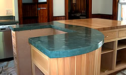 Precast concrete countertop on a teal blue color contrasts against the wood cabinets.