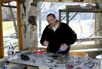 Vince Schrementi, seen here in his living room (under construction for the three years he and his family have lived in The Flintstone House) working on his mosaic, a wall of faces made out of bits of metal, glass and, of course, concrete.
