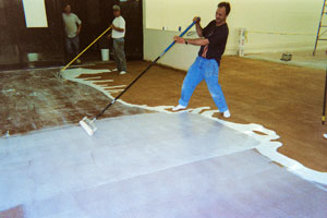 Applying Concrete Sealer with a plastic squeegee in a large room. The sealer looks white on the acid stained floor.