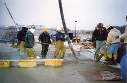Large concrete crew wading in warm water concrete placing concrete with a concrete pump.