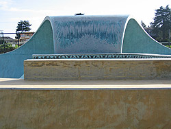 Skate park with a full pipe in the shape of a wave made from concrete.